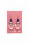 Clear glass earrings with purple tops on a beige background