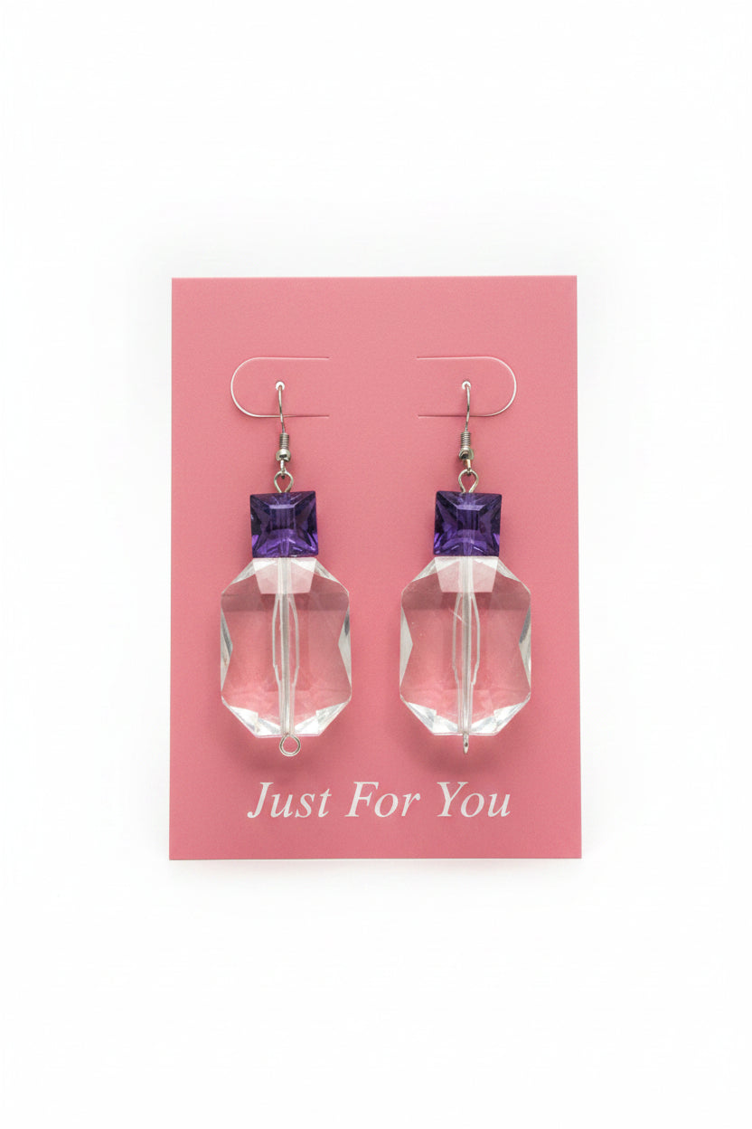 Clear glass earrings with purple tops on a beige background