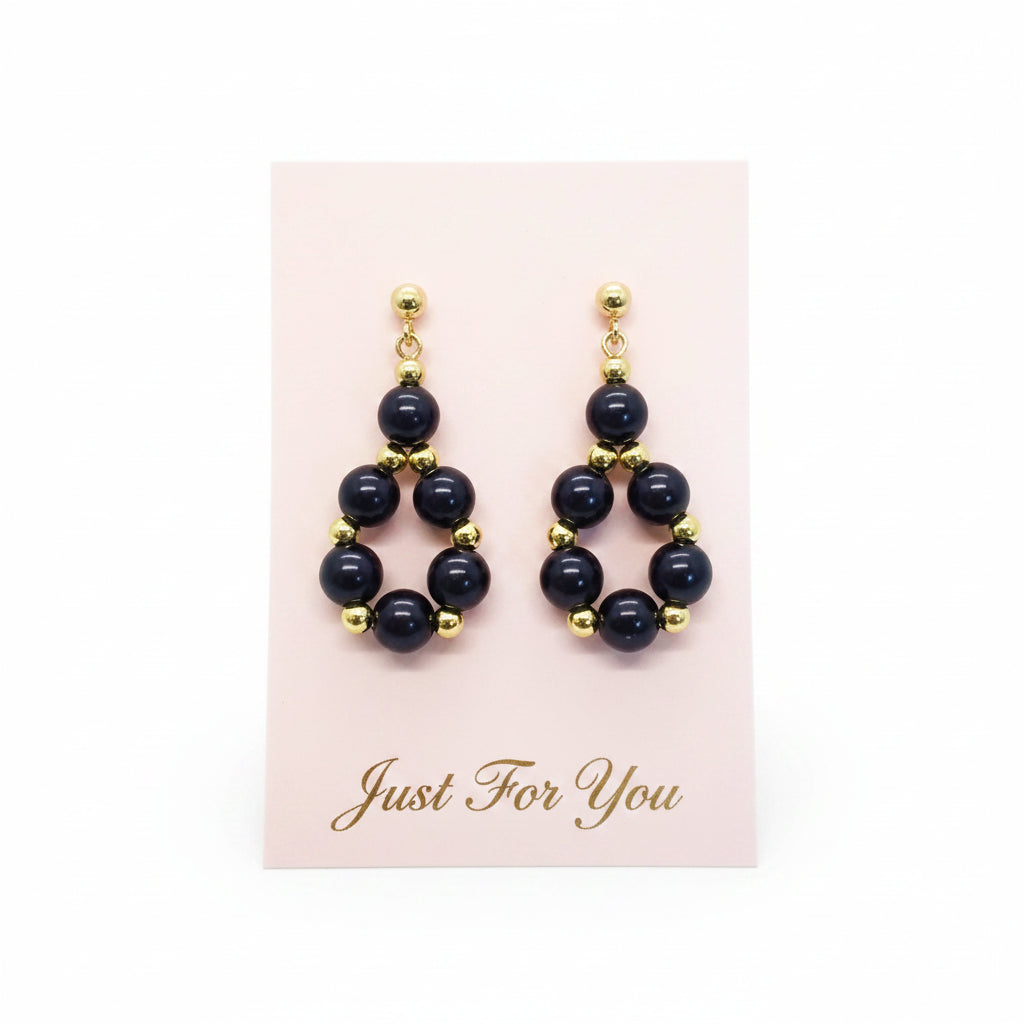 Pair of black beaded earrings with gold accents on a white card.