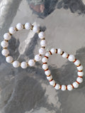 Two white beaded bracelets with gold and red accents on a textured stone surface