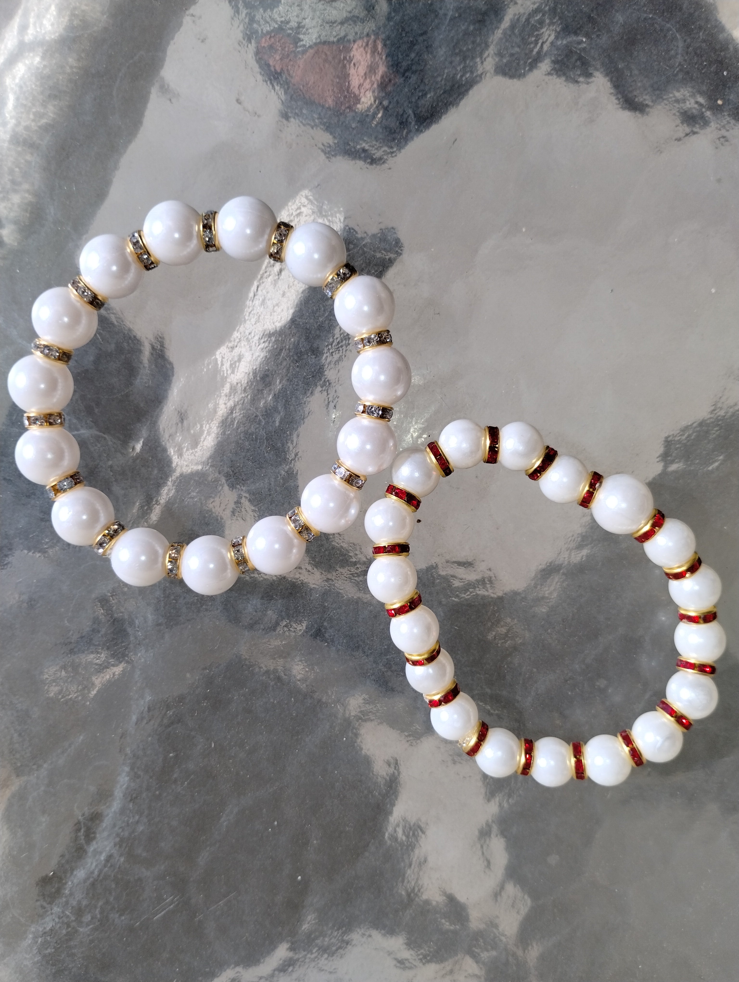Two white beaded bracelets with gold and red accents on a textured stone surface